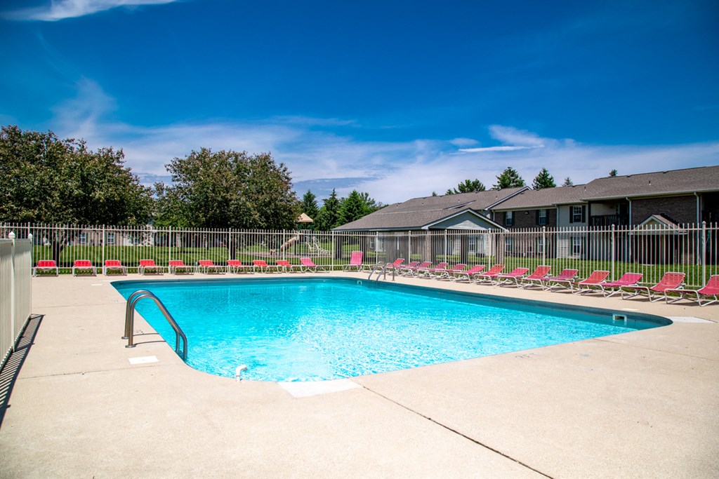 our resort style swimming pool is in front of our house with red chairs