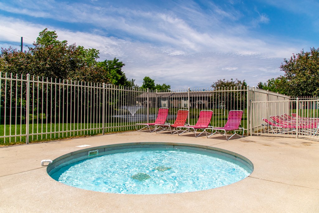 a small pool with red chairs in front of a fence