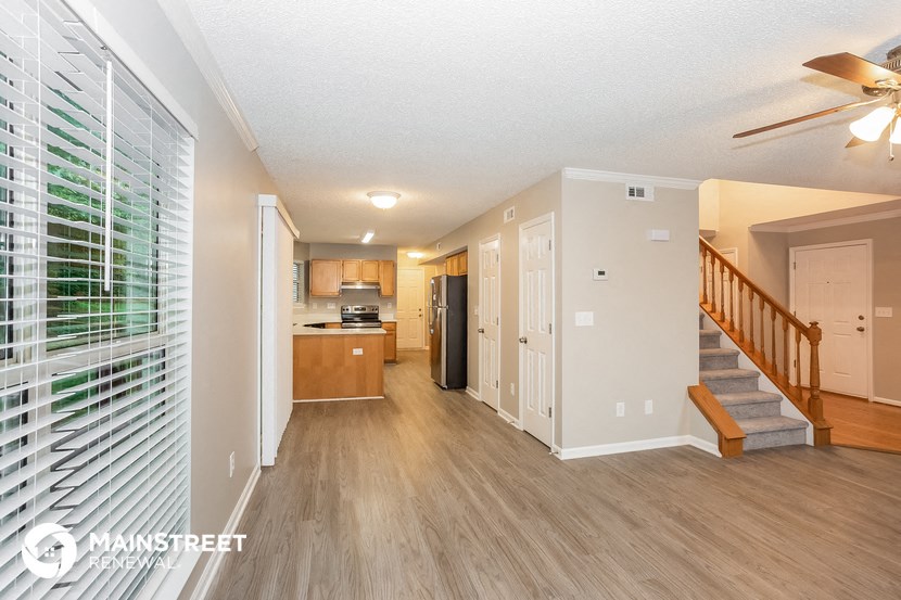 a living room with a staircase and a kitchen with a ceiling fan