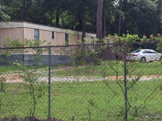 A white car is parked behind a chain link fence.