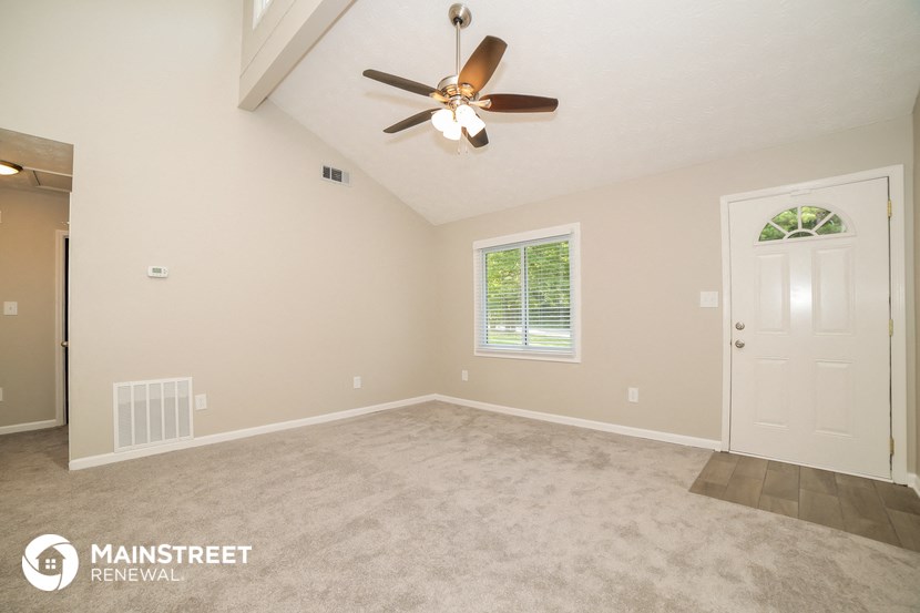 the spacious living room with ceiling fan and carpet