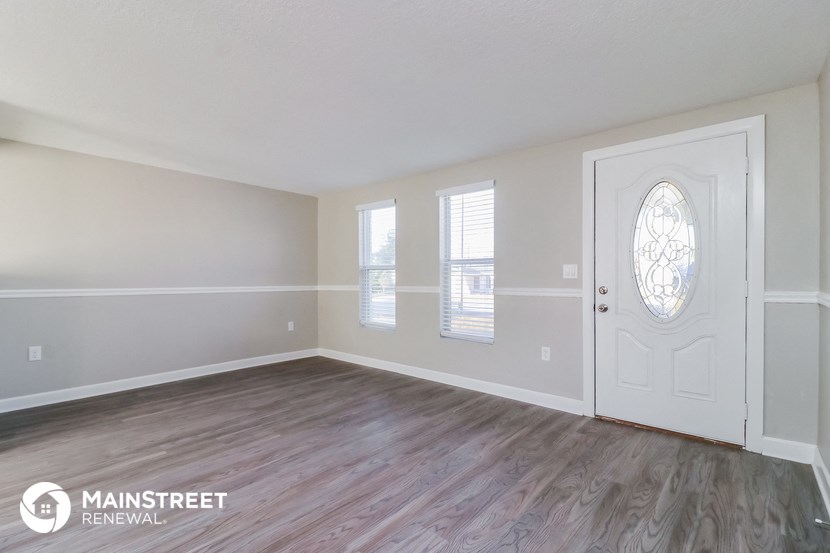 the living room of an apartment with a white door and wood floors
