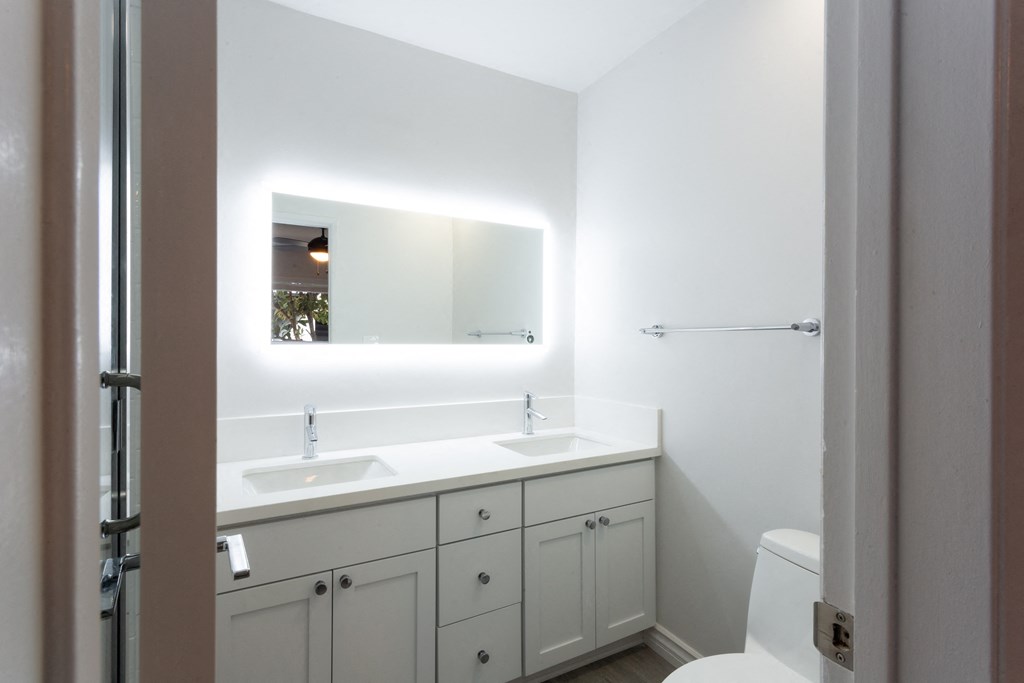 Bright bathroom in all white with light behind mirror providing ideal lighting