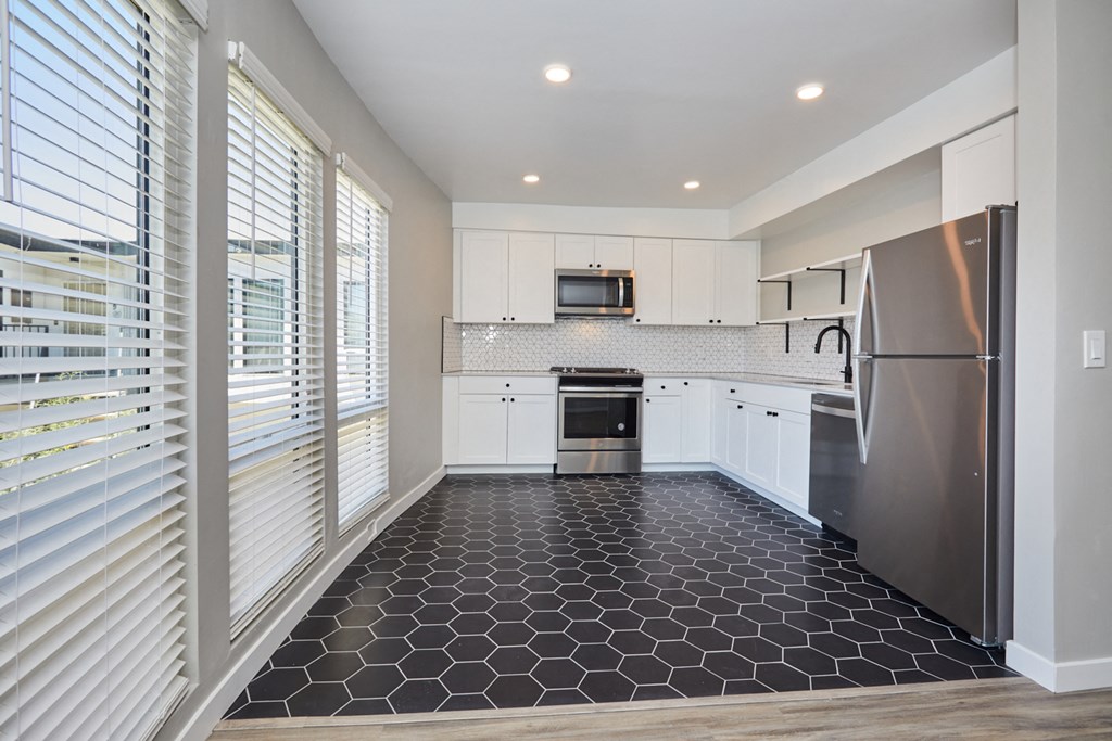 Kitchen Spacious kitchen with large windows, white walls and cabinets, and black flooring