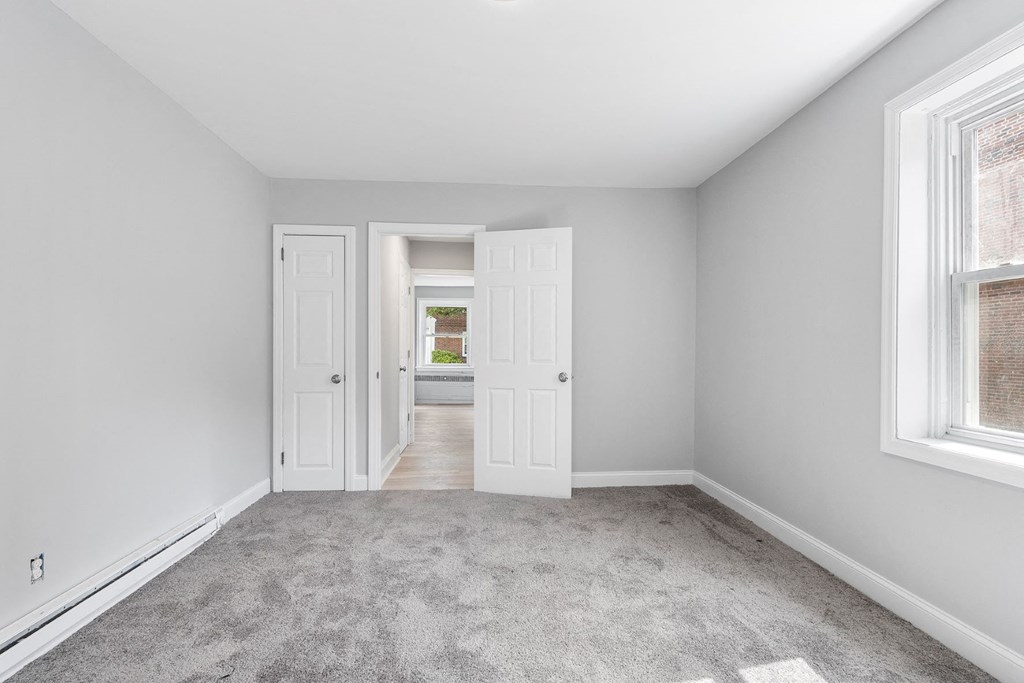 an empty bedroom with two windows and a door to a hallway