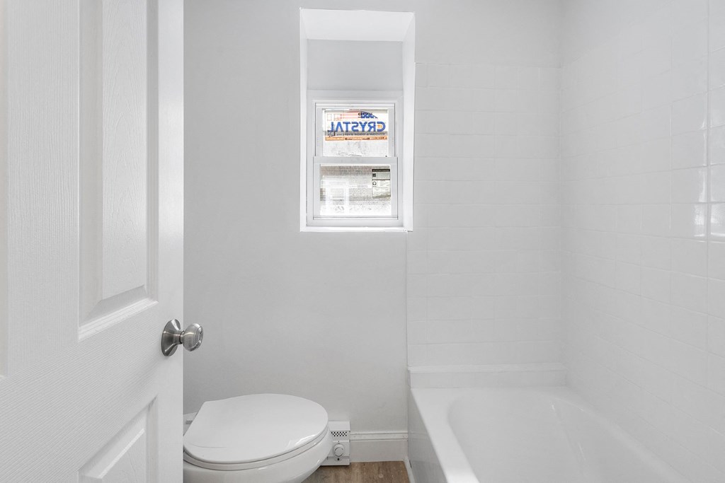 a white bathroom with a window and a toilet and a tub