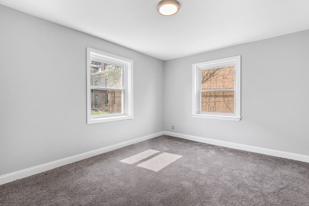 an empty room with two windows and a carpet
