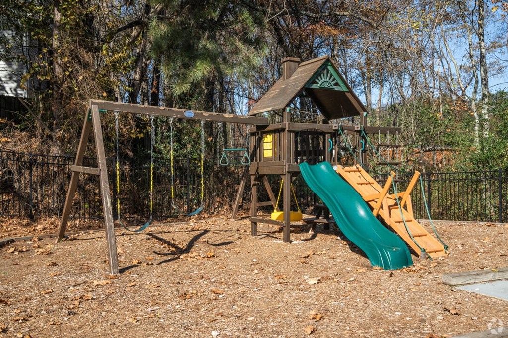 A playground with a green slide and a wooden structure.