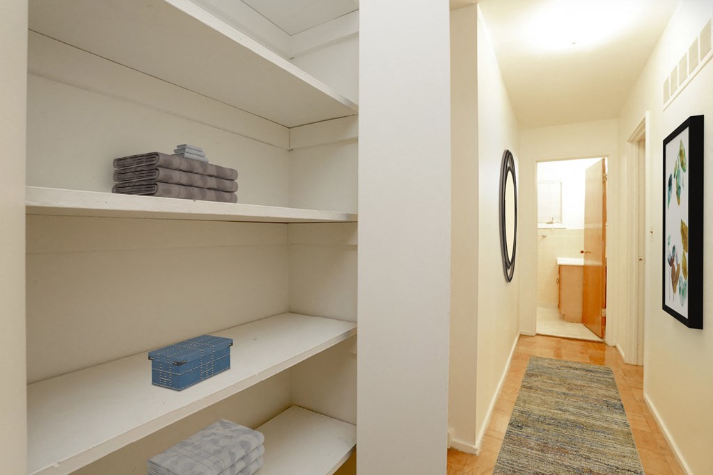 a walk in closet with white shelves and a hallway with a bathroom