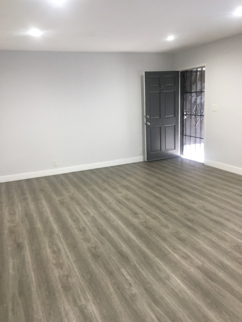 an empty living room with a wooden floor and a black door