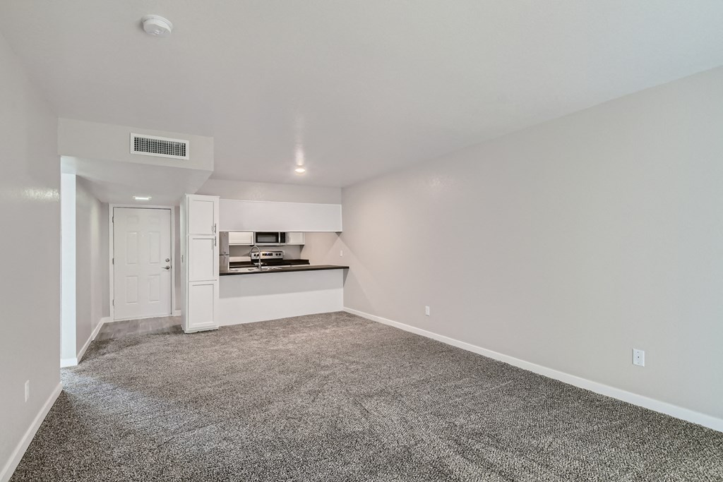 the living room and kitchen of a manufactured home with carpeting and a white kitchen