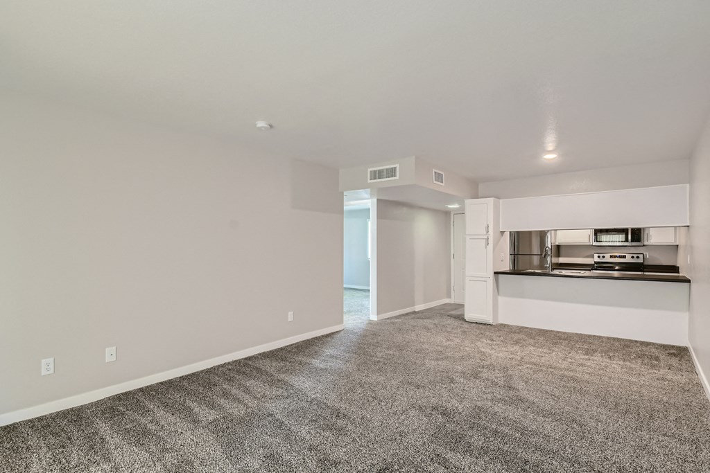 an empty living room with carpet and a kitchen