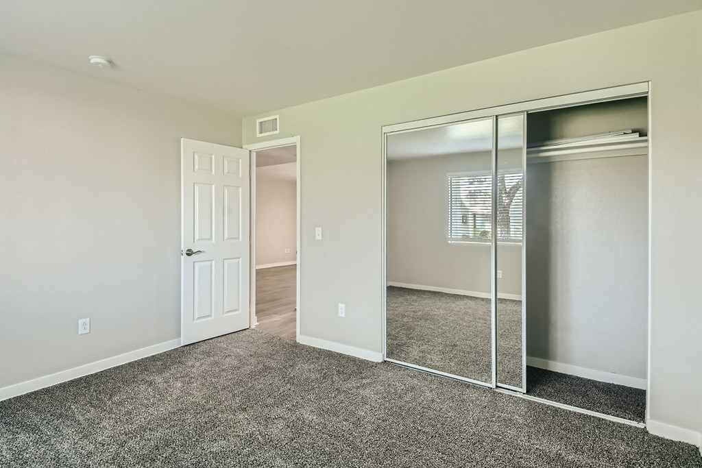 an empty bedroom with mirrored closet doors and carpeting