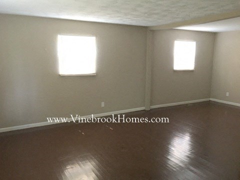 an empty living room with a wooden floor and two windows