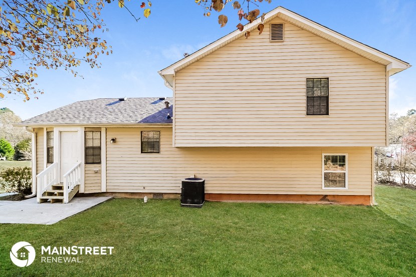 the front of a white house with a yard and a trash can