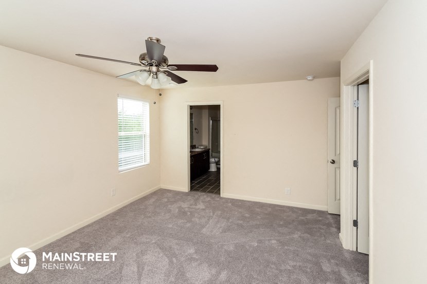 an empty living room with a ceiling fan and a door to a bathroom