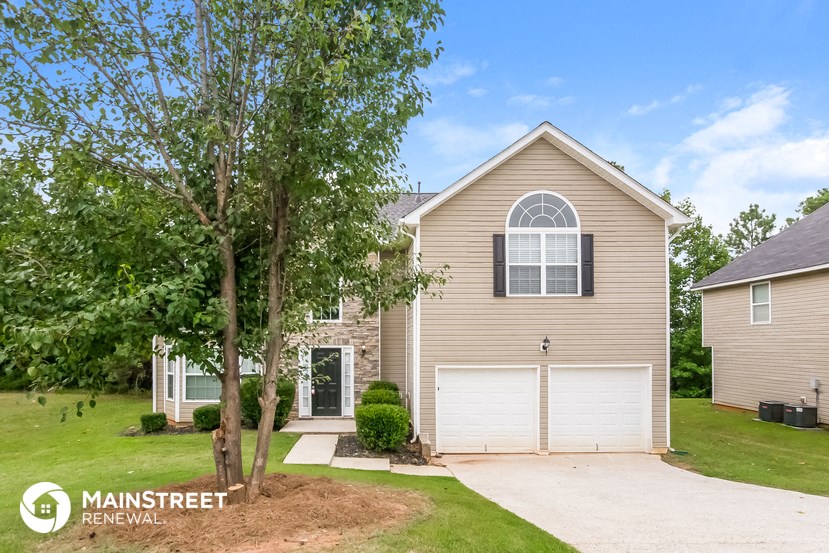 a beige house with a white garage door and a tree