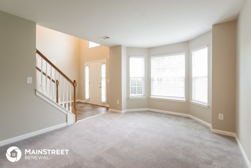 an empty living room with a staircase and large windows