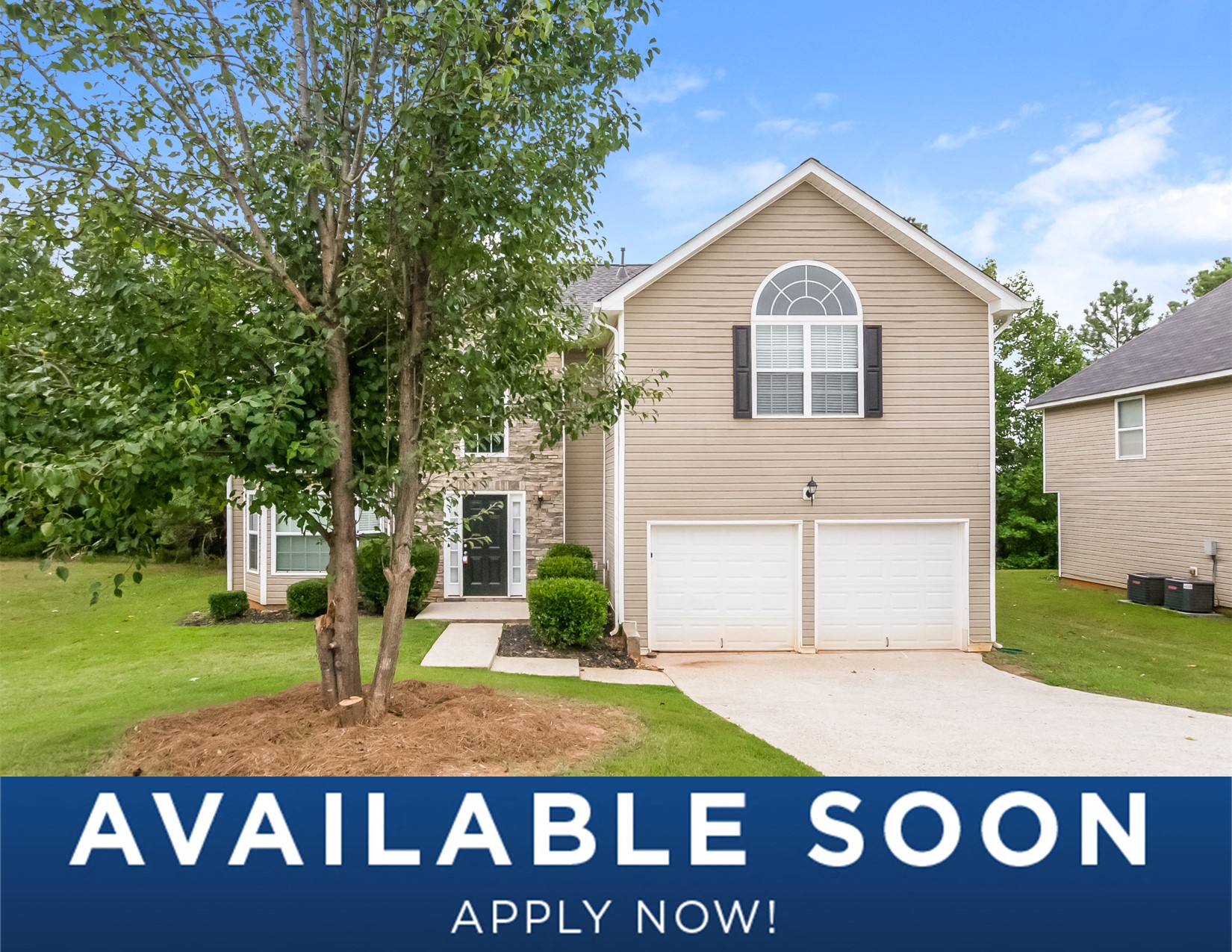 a beige house with a tree and a driveway