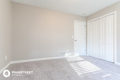 the bedroom of a manufactured home with white doors and carpet