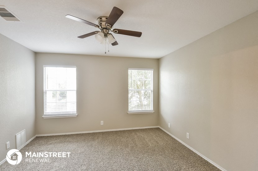 an empty room with a ceiling fan and two windows