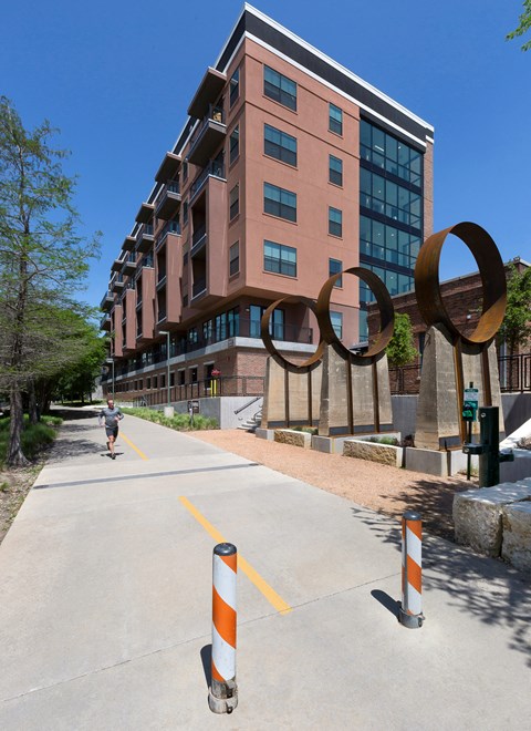 a person walking down a sidewalk in front of a building with an art sculpture on