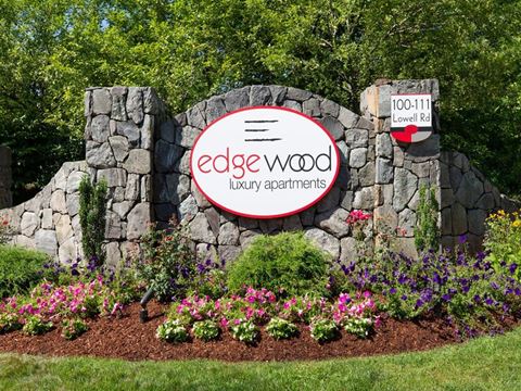 a sign for edge wood luxury apartments in front of a stone wall and flowers
