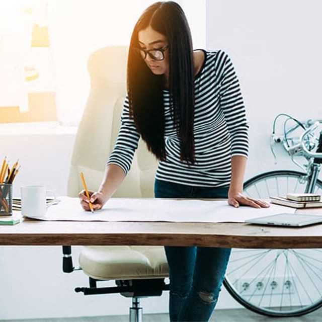 a woman writing on a large paper on a desk