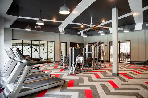 a gym with cardio machines and a ceiling fan