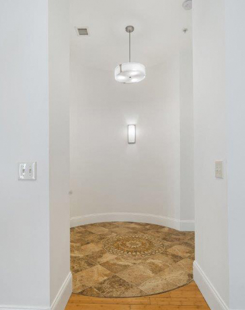 an empty room with white walls and a round rug and a light hanging on the