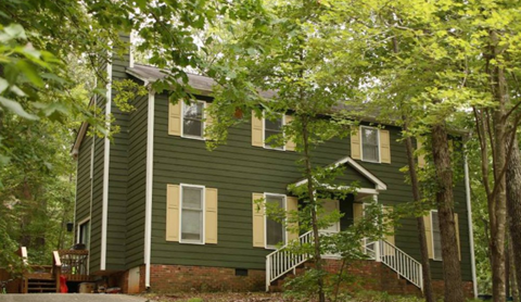 A green house with a porch and a tree in front.