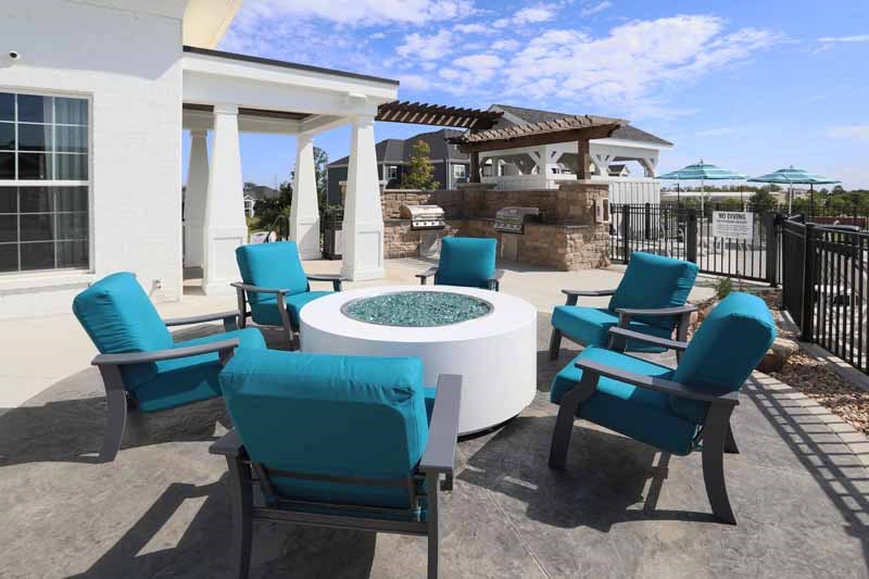 a patio with blue chairs and a fire pit