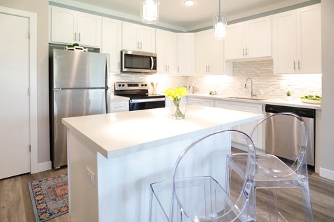 a white kitchen with a white island and transparent chairs