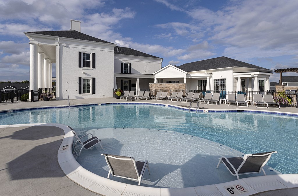 a large swimming pool with chairs in front of a house