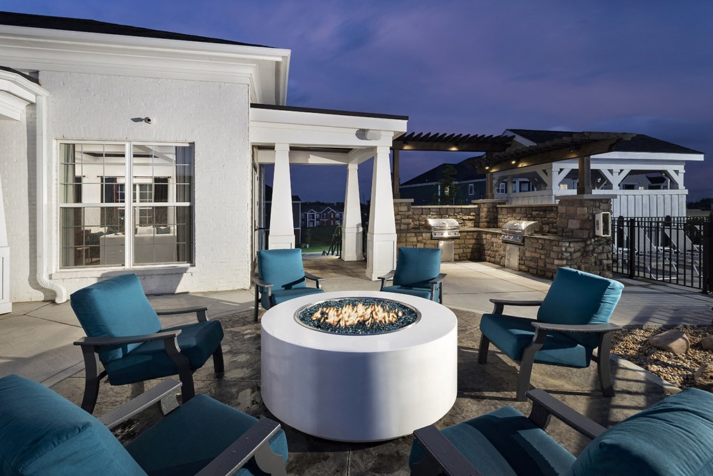 a patio with chairs and a fire pit at night