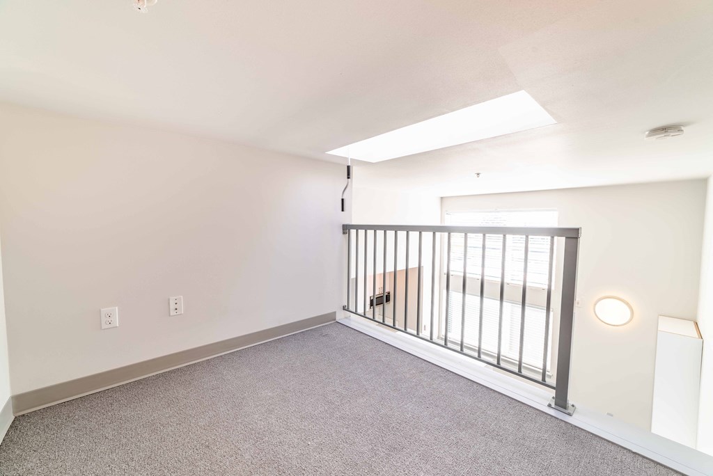 the upstairs loft of a home with white walls and carpeting and a railing