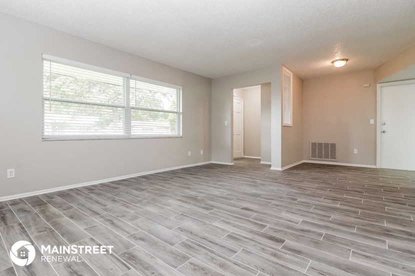 the living room of an apartment with a large window and wood flooring