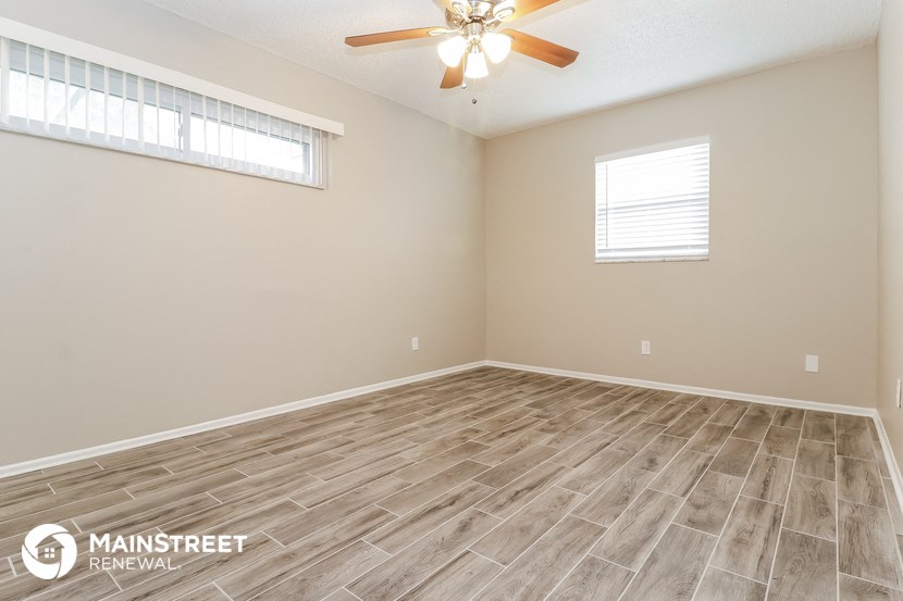 the spacious living room with wood flooring and a ceiling fan