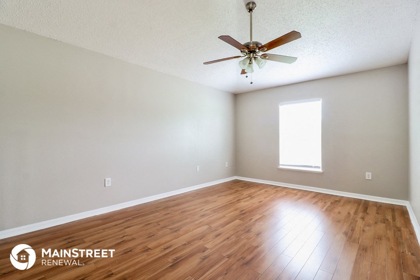 the spacious living room with hardwood floors and a ceiling fan