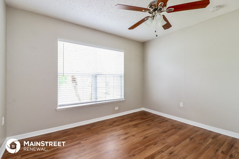 the spacious living room with hardwood flooring and a ceiling fan