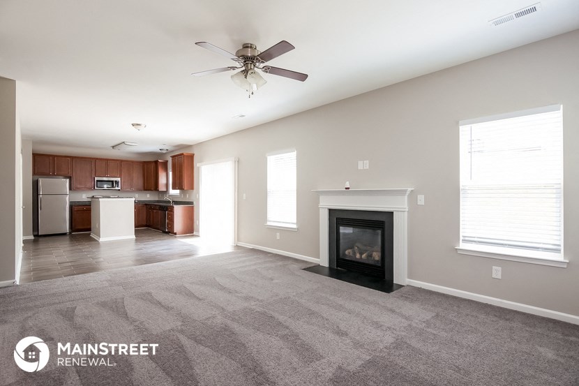 an empty living room with a fireplace and a kitchen