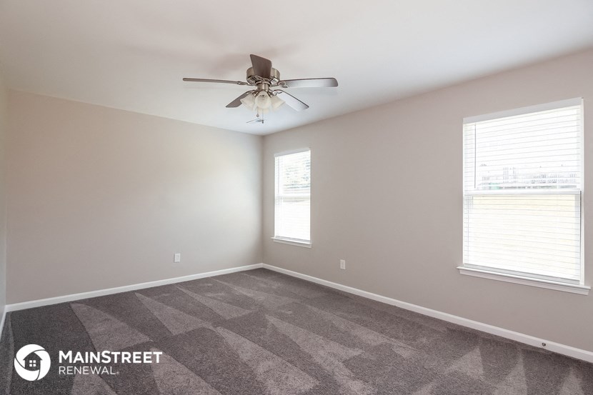 the spacious living room with carpeted flooring and a ceiling fan