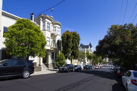 A street view with cars parked on the side and a white building with a tower in the background.