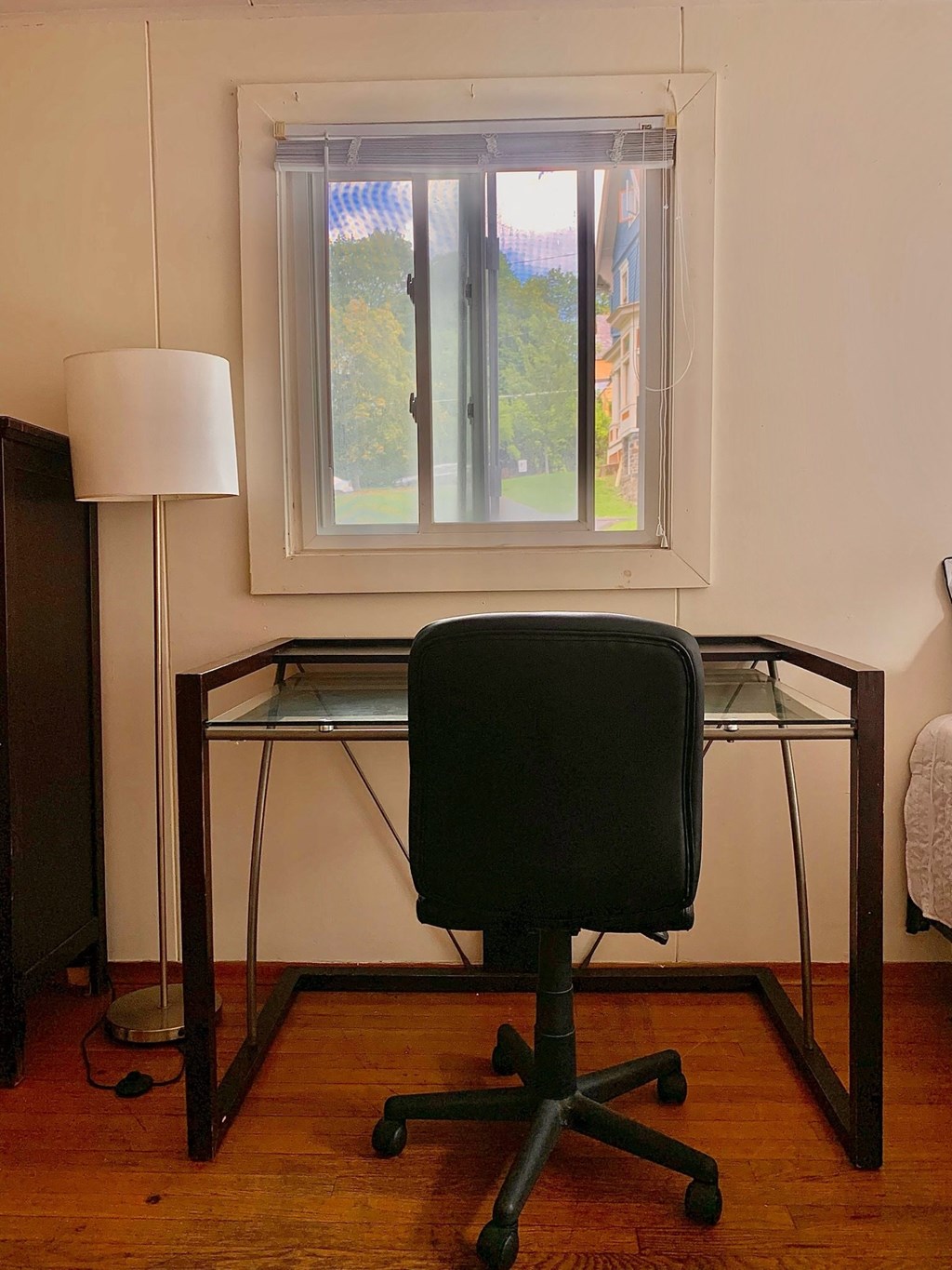 A black chair sits in front of a desk with a lamp and a window in the background.