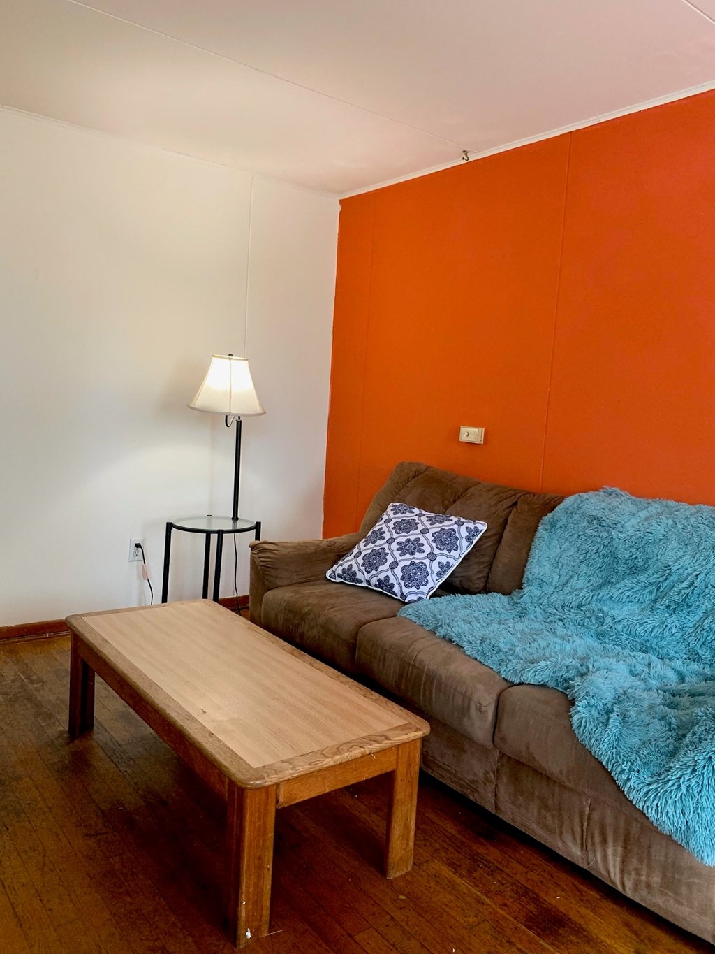 A lamp stands on a black stand next to a couch with a blue throw on it.