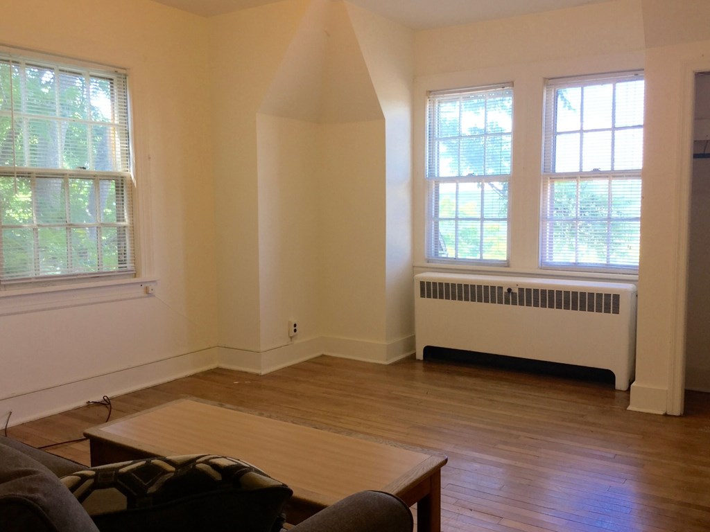A living room with a brown wooden floor and a white radiator beneath a window.