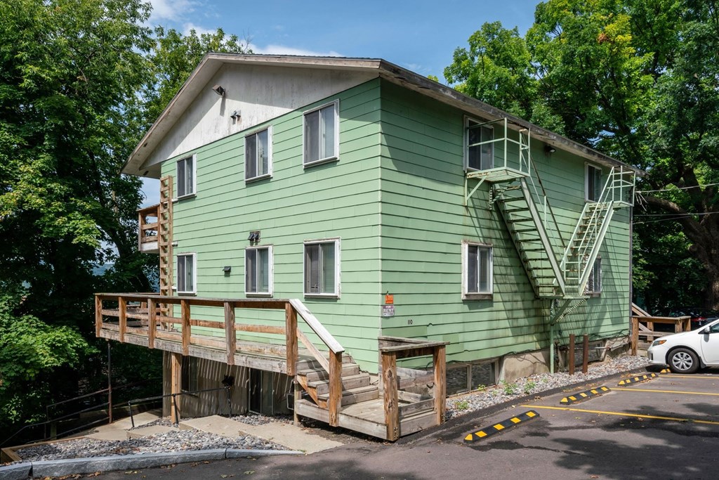 A green house with a wooden deck and stairs leading to the second floor.