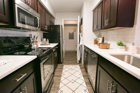 a kitchen with black appliances and white counters and dark wood cabinets