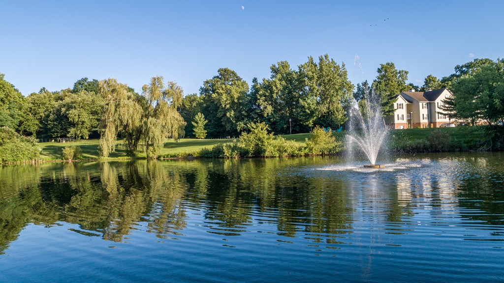 a fountain in the middle of a lake with a house in the background