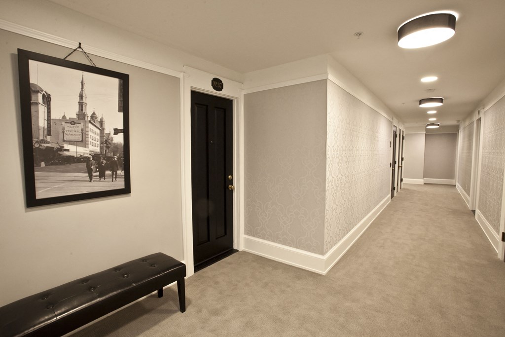 a long hallway with a bench and a picture on the wall and a black door